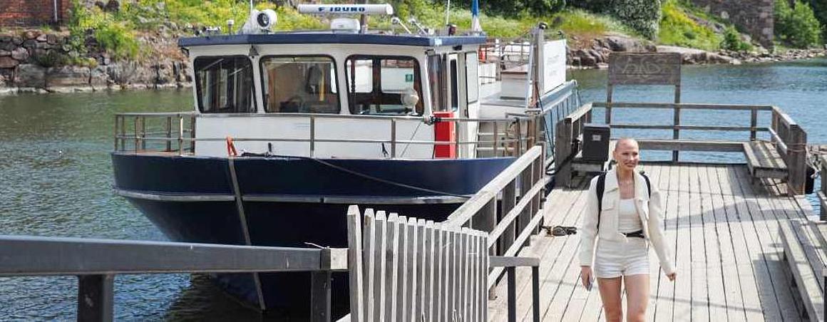 A boat is lying on the dock and a woman is walking on the dock. The sun is shining.