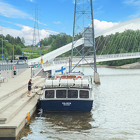 A boat is lying at the pier, behind the boat is a bridge. 