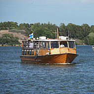 An old wooden boat drives in front of the island, which is surrounded by the sea.