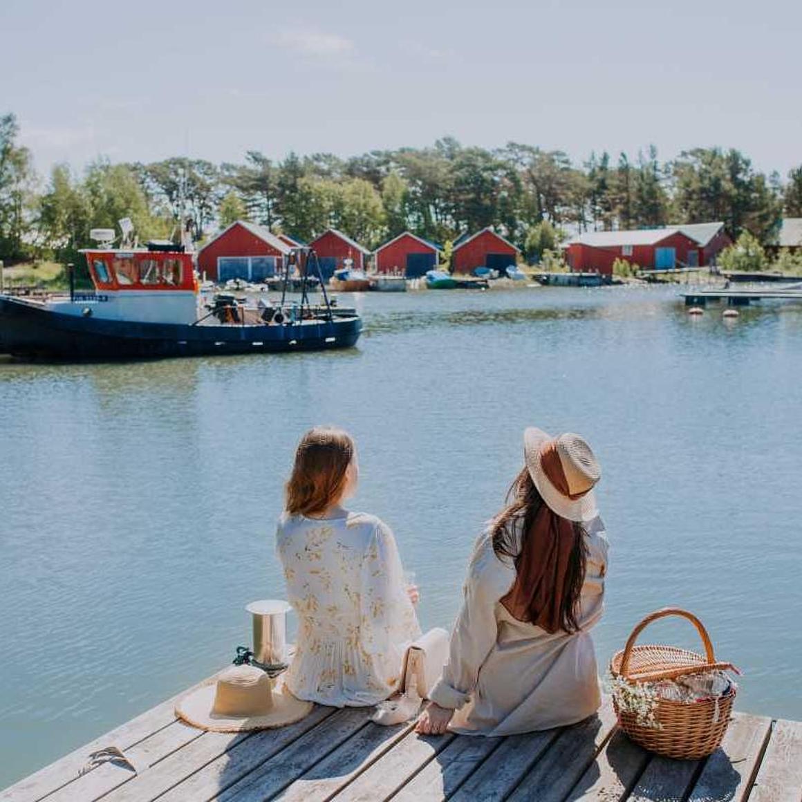 Two girls are sitting in the harbor and enjoy the view to wooden red houses.