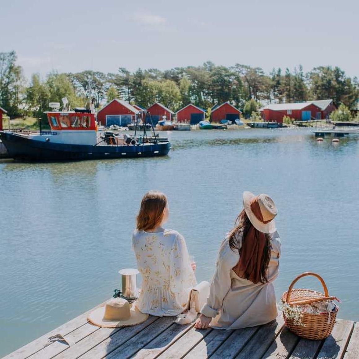 Two girls are sitting in the harbor and enjoy the view to wooden red houses.