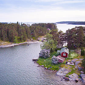 The drone image shows an archipelago of red wooden houses and forests.
