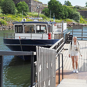 A boat is lying on the dock and a woman is walking on the dock. The sun is shining. 