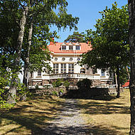 An old villa is seen, sourounded by a lot of old and big trees. 