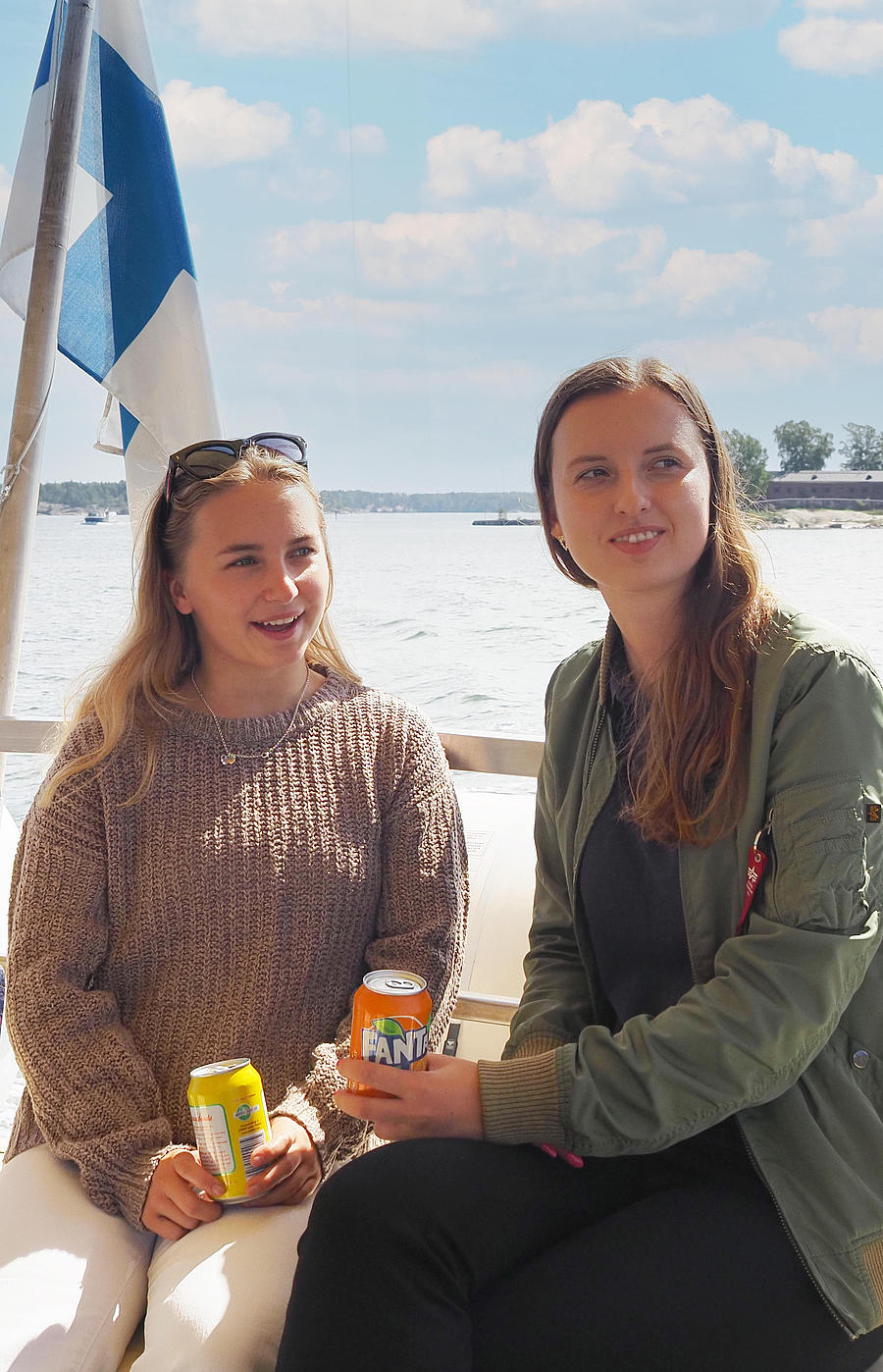 Two women are sitting on the railing of a boat, enjoying a drink.