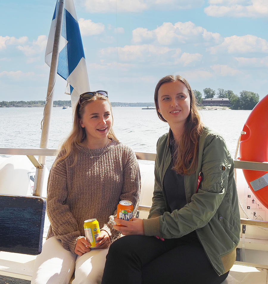 Two women are sitting on the railing of a boat, enjoying a drink.