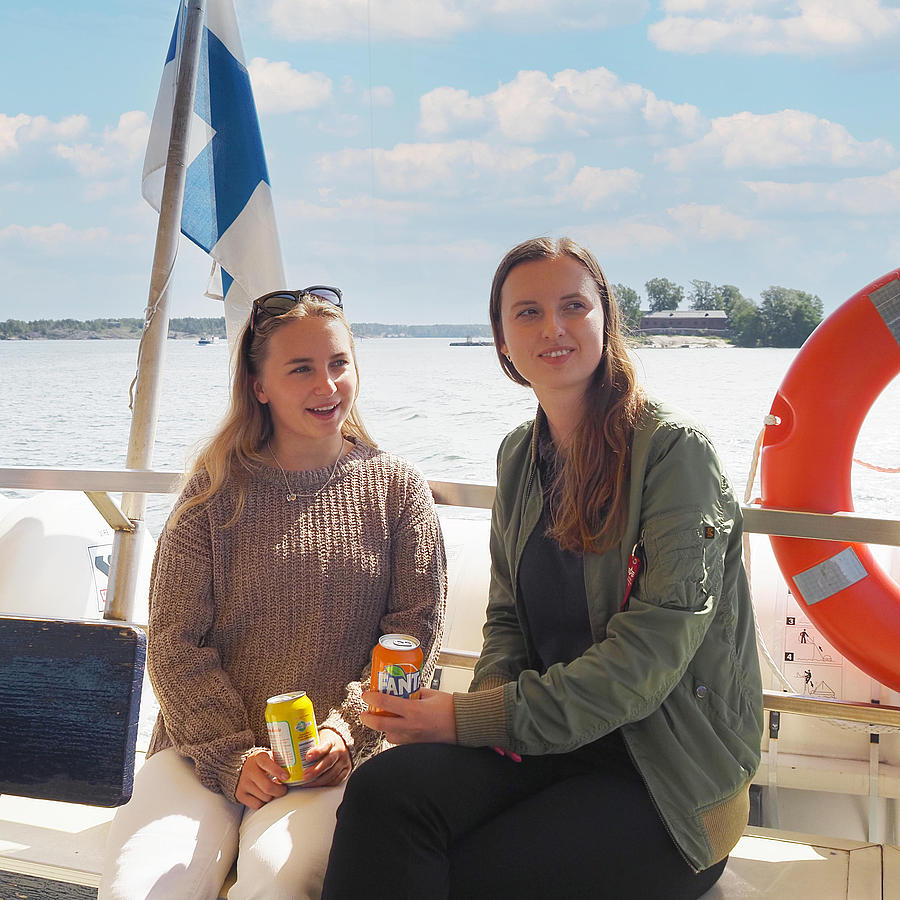 Two women are sitting on the railing of a boat, enjoying a drink.