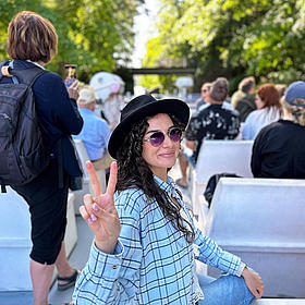 A woman is sitting on the deck of a ferry and is having a look to the camera. 