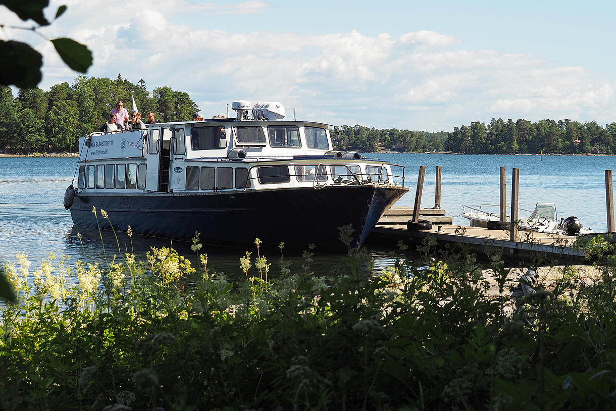 View of a ferry on the sea surrounded by lush island scenery.