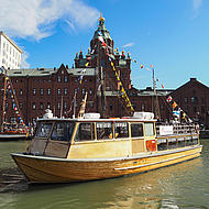 An old wooden ship sails in the harbour, decorated with colourful little flags.