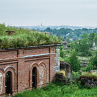 An old brick building surrounded by greenery, overlooking the sea.